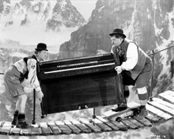 Laurel and Hardy moving a piano over a narrow footbridge in the Alps